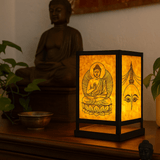 A glowing square Lokta paper lantern with traditional Buddhist artwork softly illuminates a spiritual corner featuring wall hangings and a floor cushion.